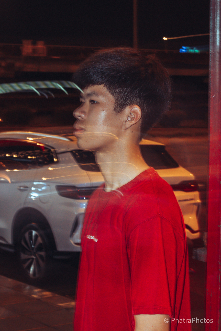 Portrait in a red shirt, shot through glass at night